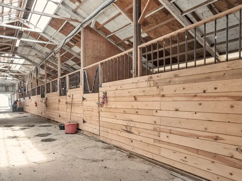 A long barn aisle with wooden stall fronts under skylights