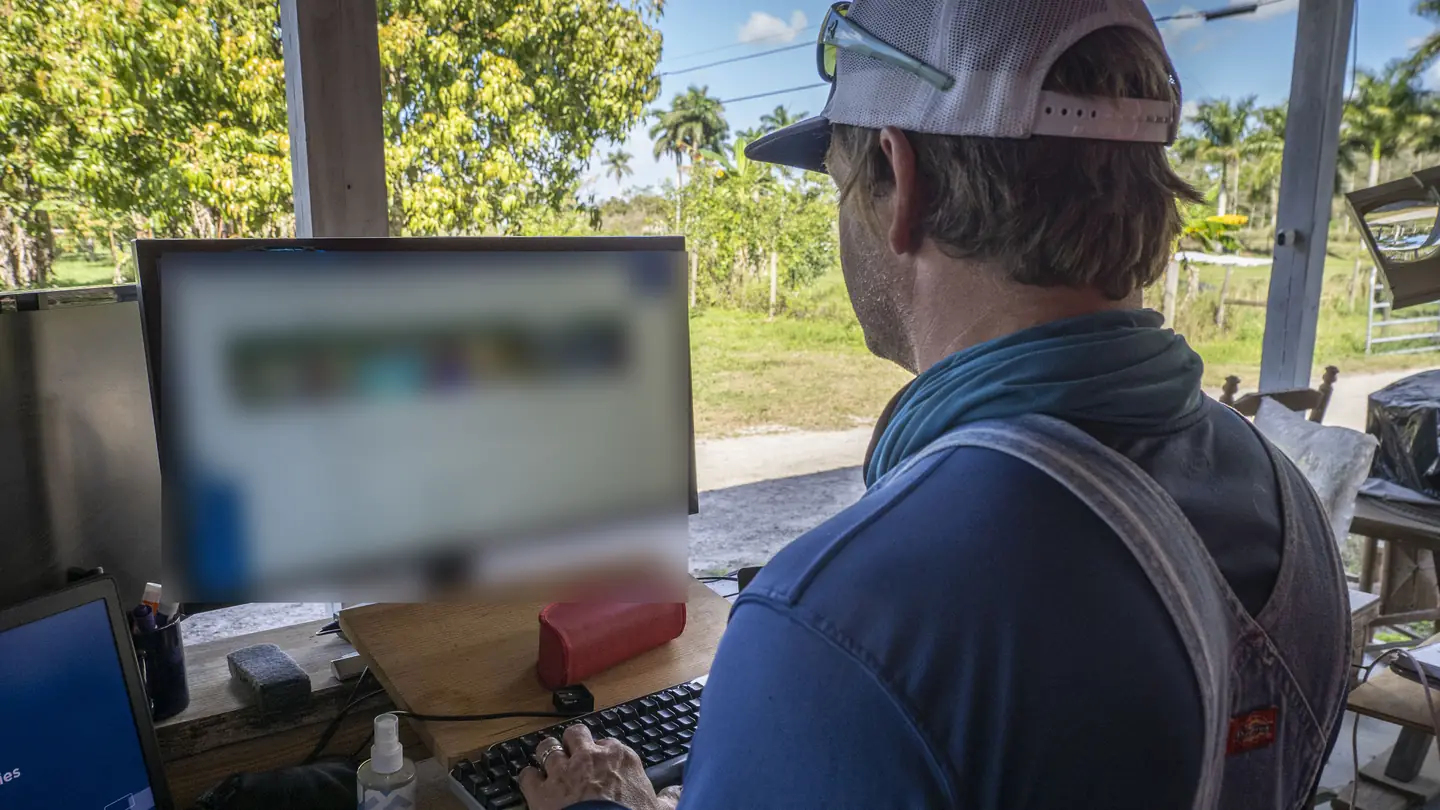A farmer typing at a desk computer under a covered farm shed