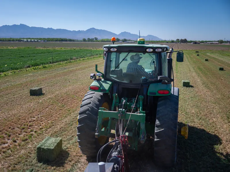 A tractor baling hay in a field below the mountains