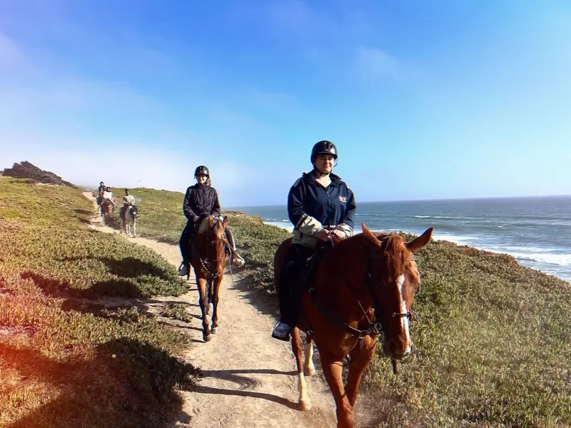 Two riders in helmets coming up a coastal trail above the ocean