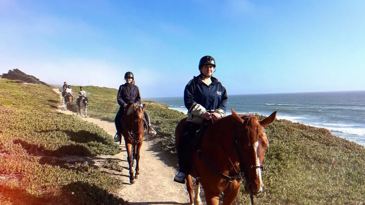 Two riders in helmets coming up a coastal trail above the ocean