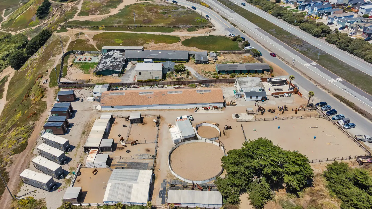 A horse ranch on a coastal bluff seen from the air, with guest pods along its edge