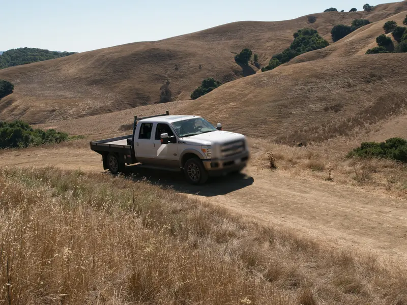 A flatbed pickup on a dirt ranch road through golden summer hills